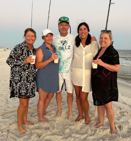 Group of five guests with drinks and fishing rods in the sand at golden hour on a shark fishing trip in Gulf Shores, Alabama