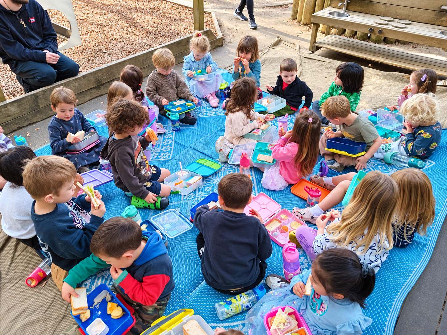 Children eating lunch together outside on mats