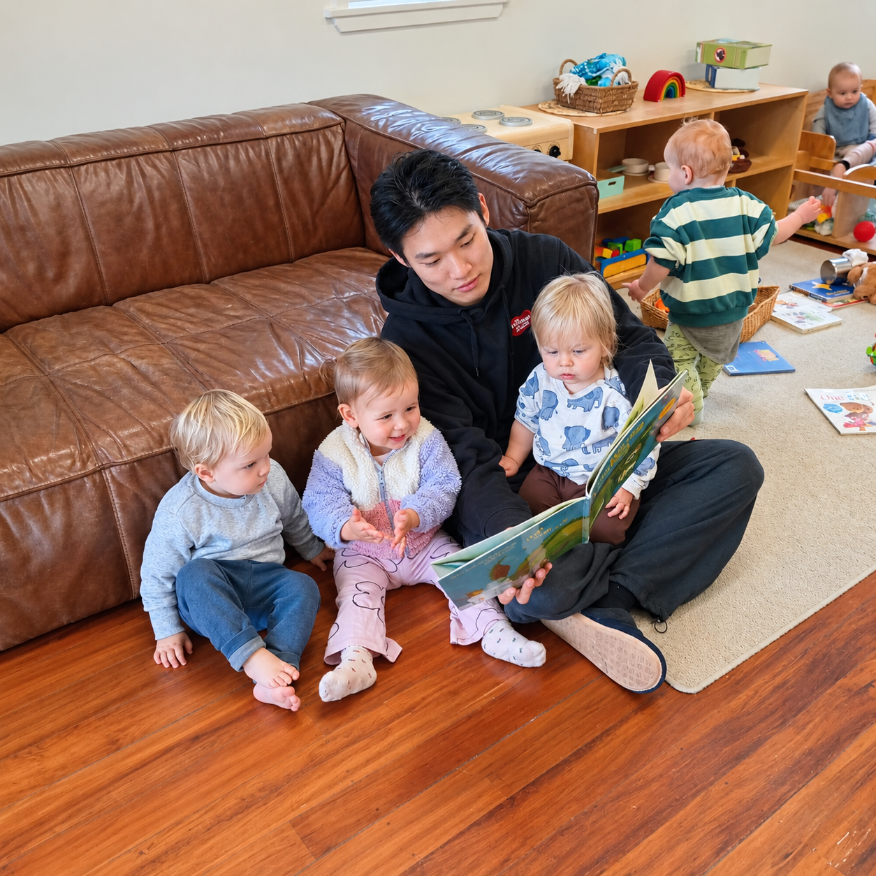 Teacher reading a picture book to toddlers in the Nest room