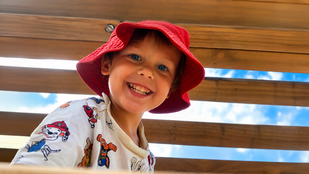 Smiling child wearing a red bucket hat at the playground