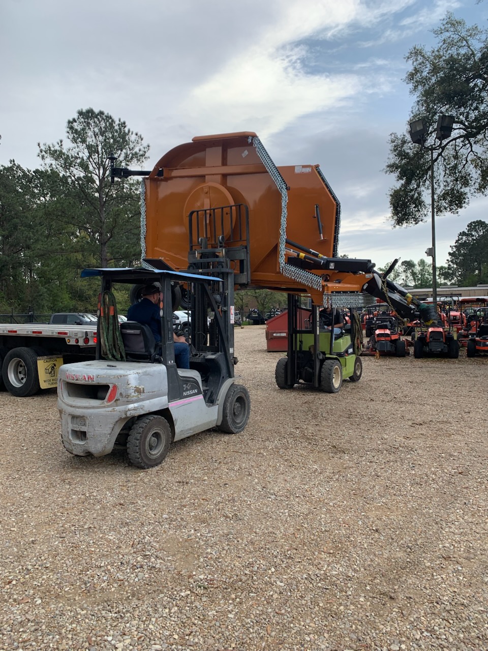 Evergreen Tractor staff loading a heavy-duty mower attachment with forklifts