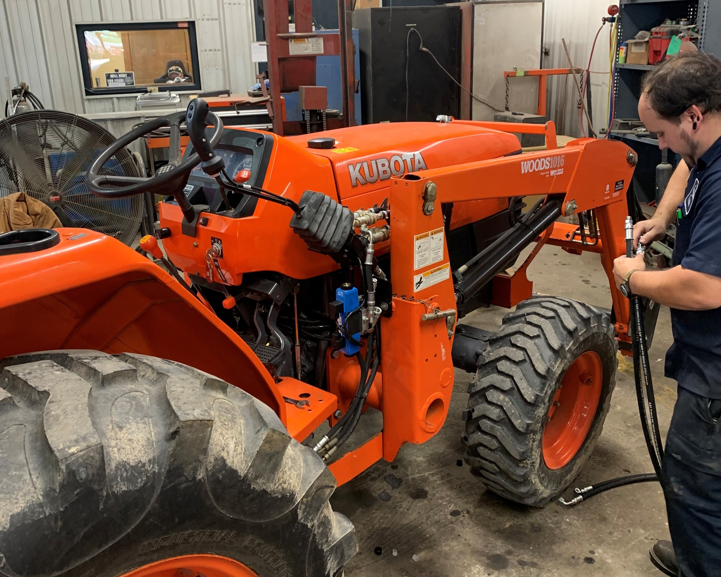 Evergreen Tractor technician inspecting hydraulic lines on a Kubota tractor in the service workshop
