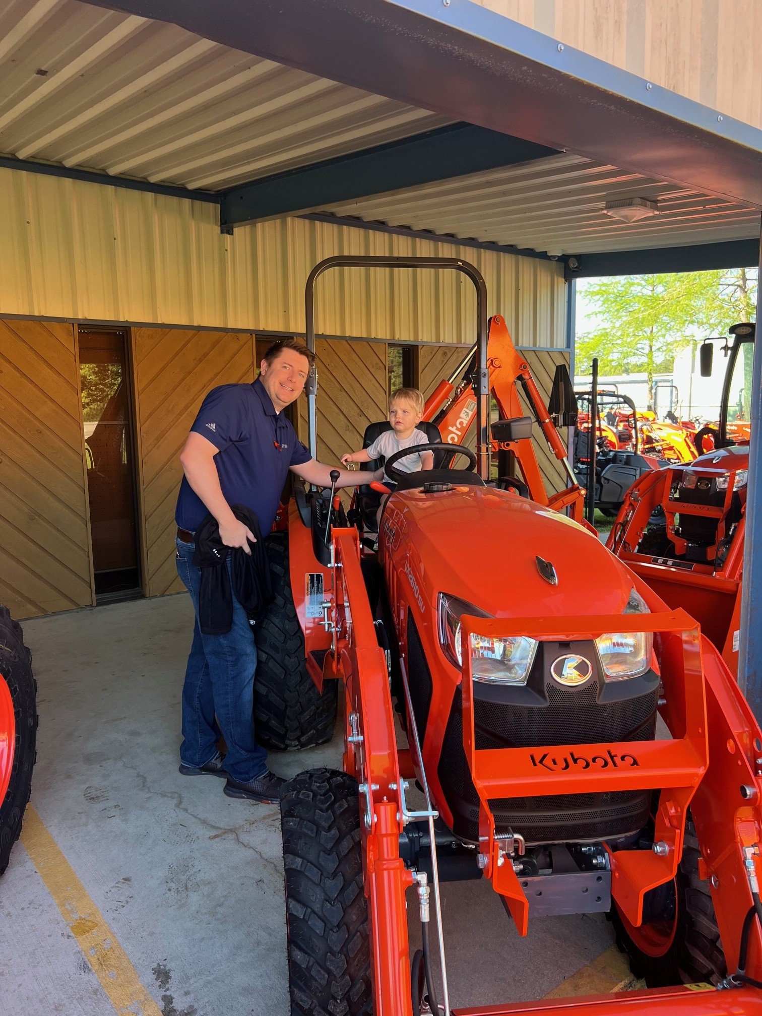 Evergreen Tractor team member helping a young child sit in the driver's seat of a Kubota tractor at the dealership open house