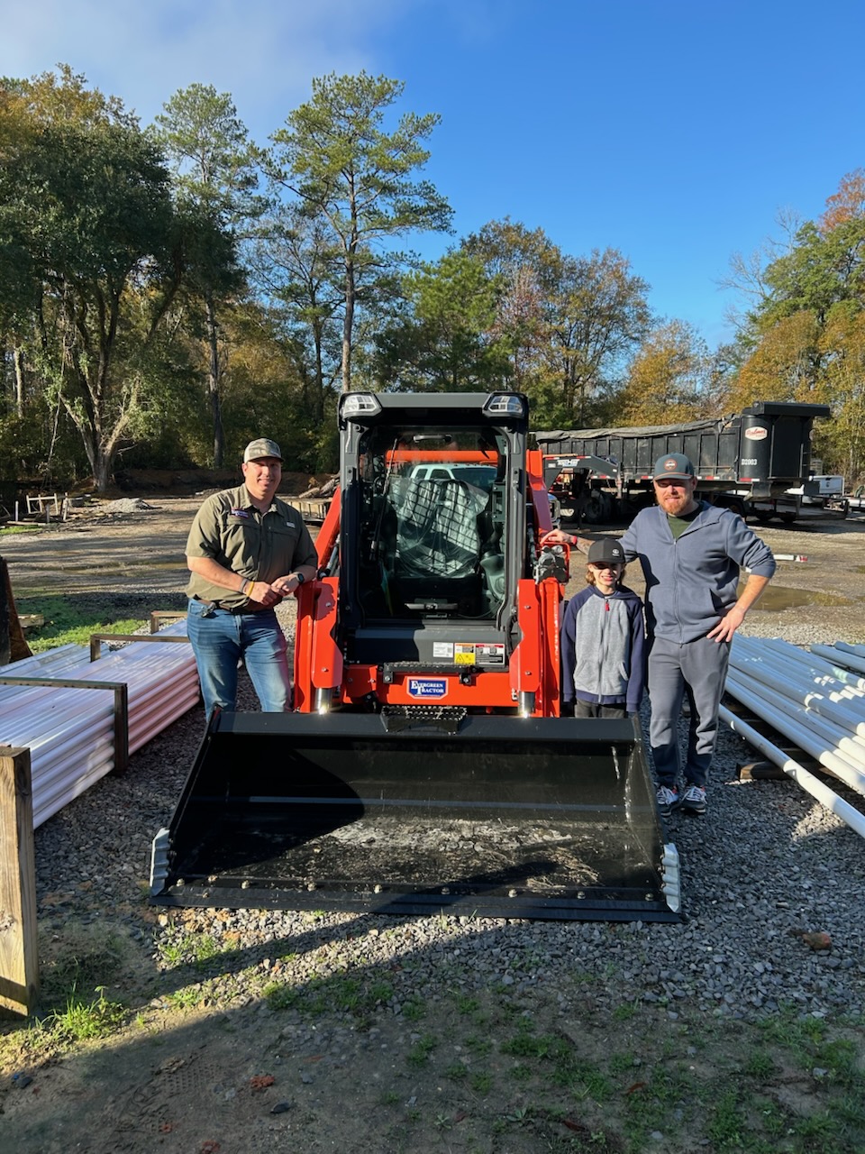 Family posing in front of their new orange Kubota skid steer loader