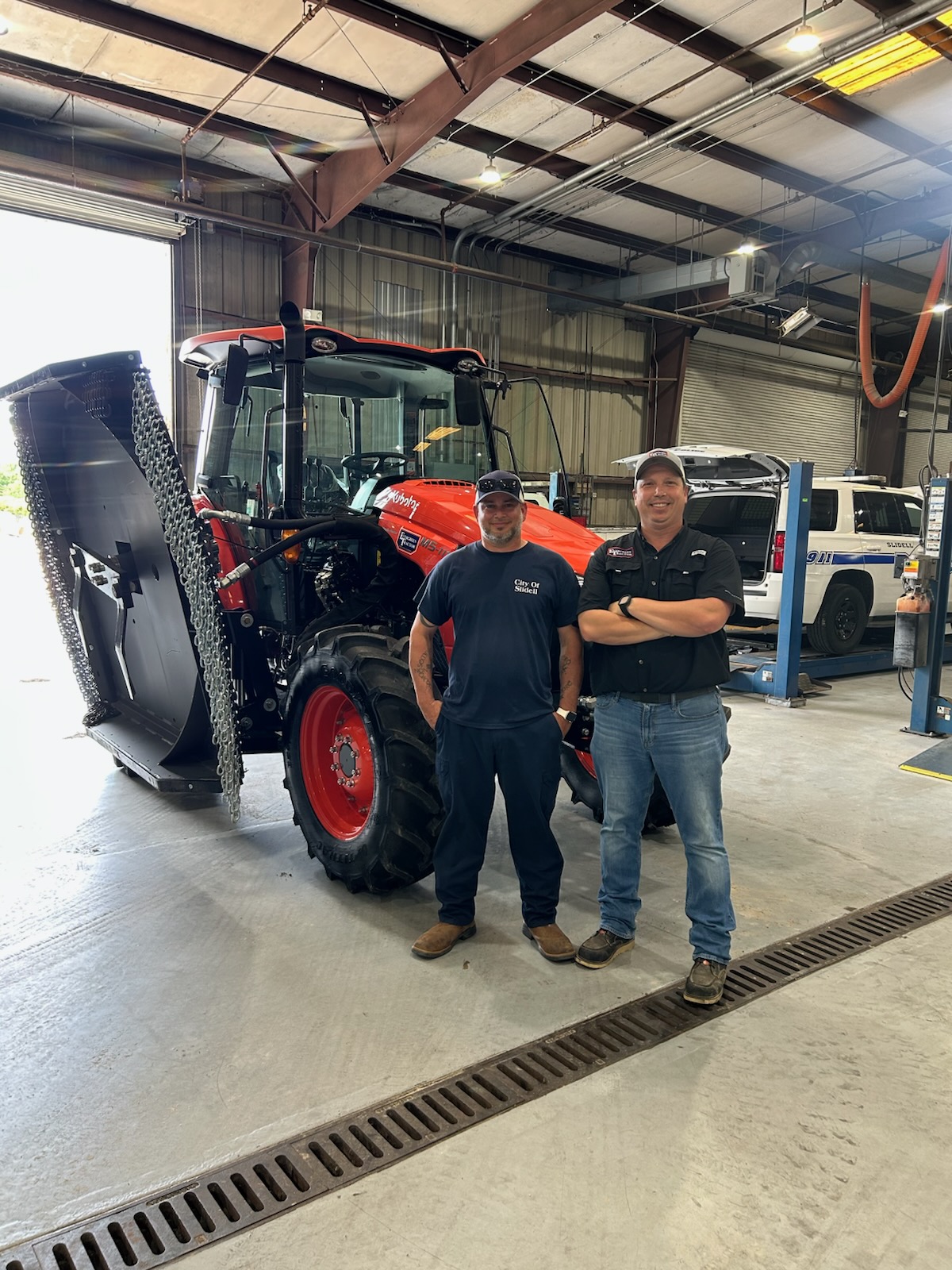 Evergreen Tractor technician with City of Slidell staff beside a Kubota tractor with boom mower in their service bay