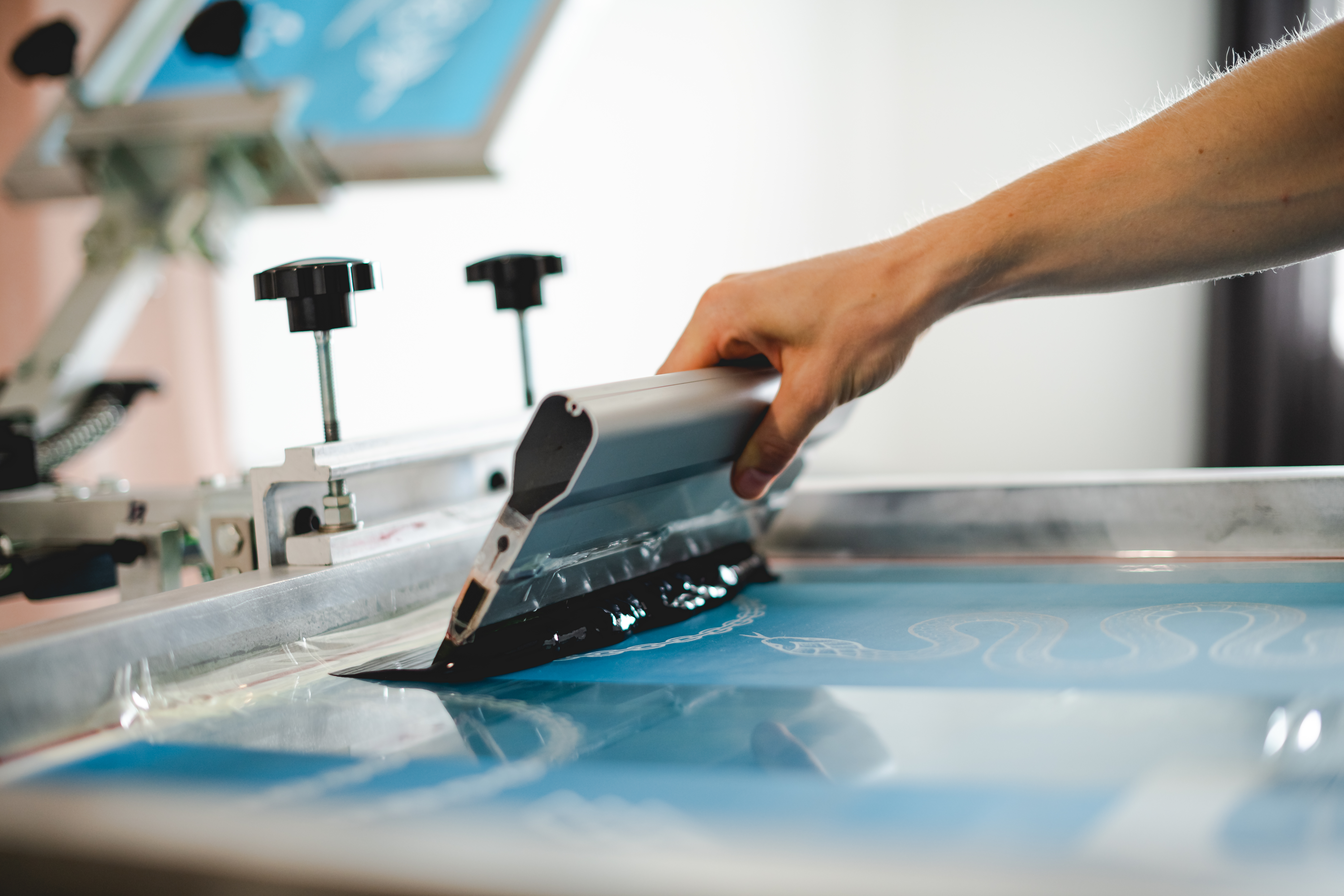 Close-up of screen printing squeegee pulling black ink across a silkscreen mesh
