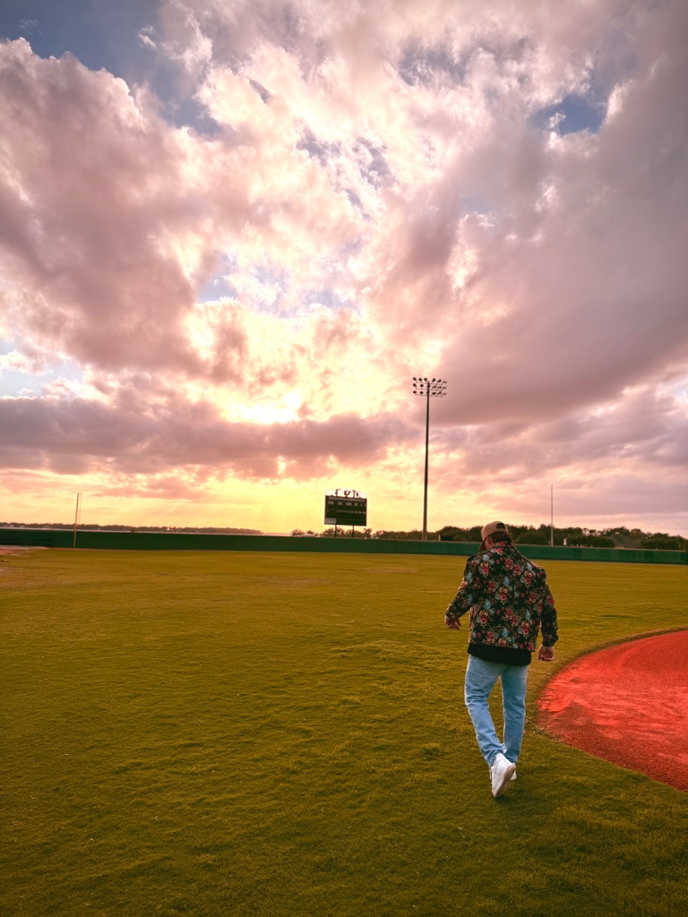 Cody walking on a baseball field under a dramatic sunset sky