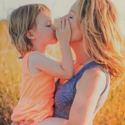 A mother and young daughter sharing a tender kiss at golden hour