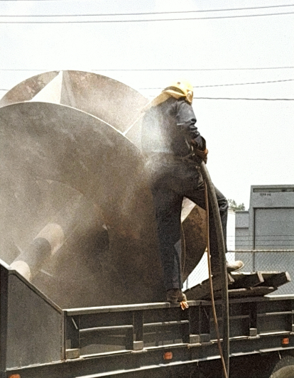 Worker sandblasting fabricated component on truck