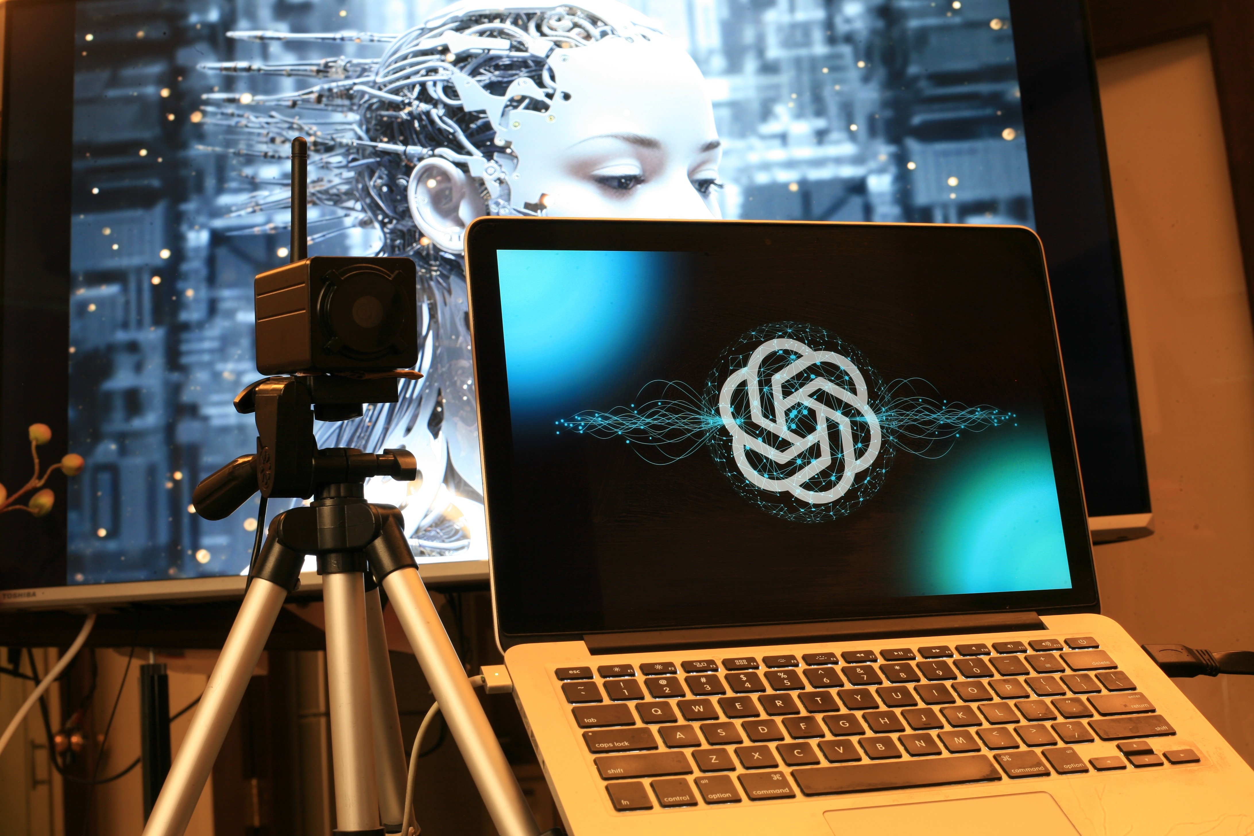 Open laptop with glowing ChatGPT logo and large screen displaying a cyborg head, symbolising AI warning signs