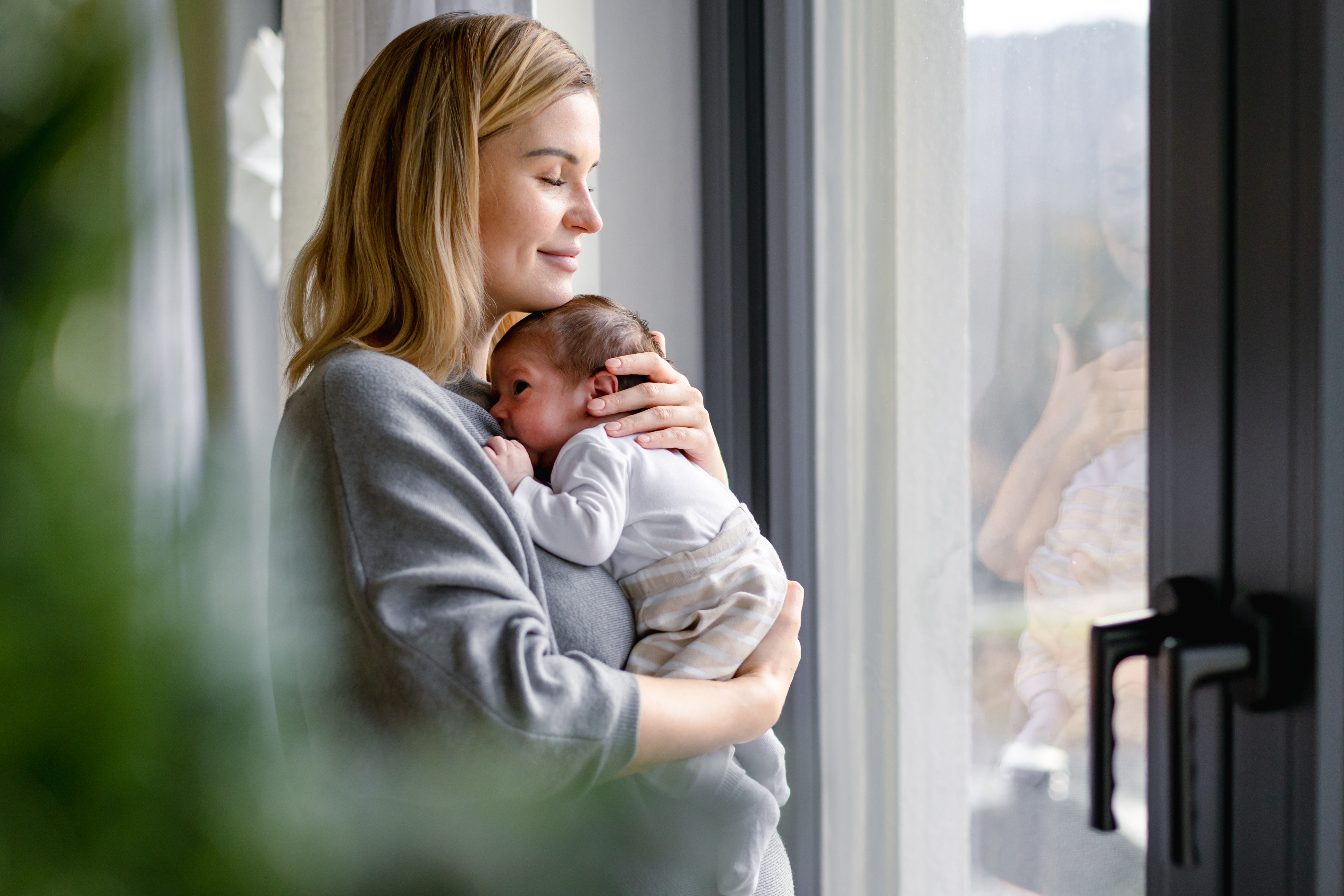 Mother cradling her newborn near a bright window