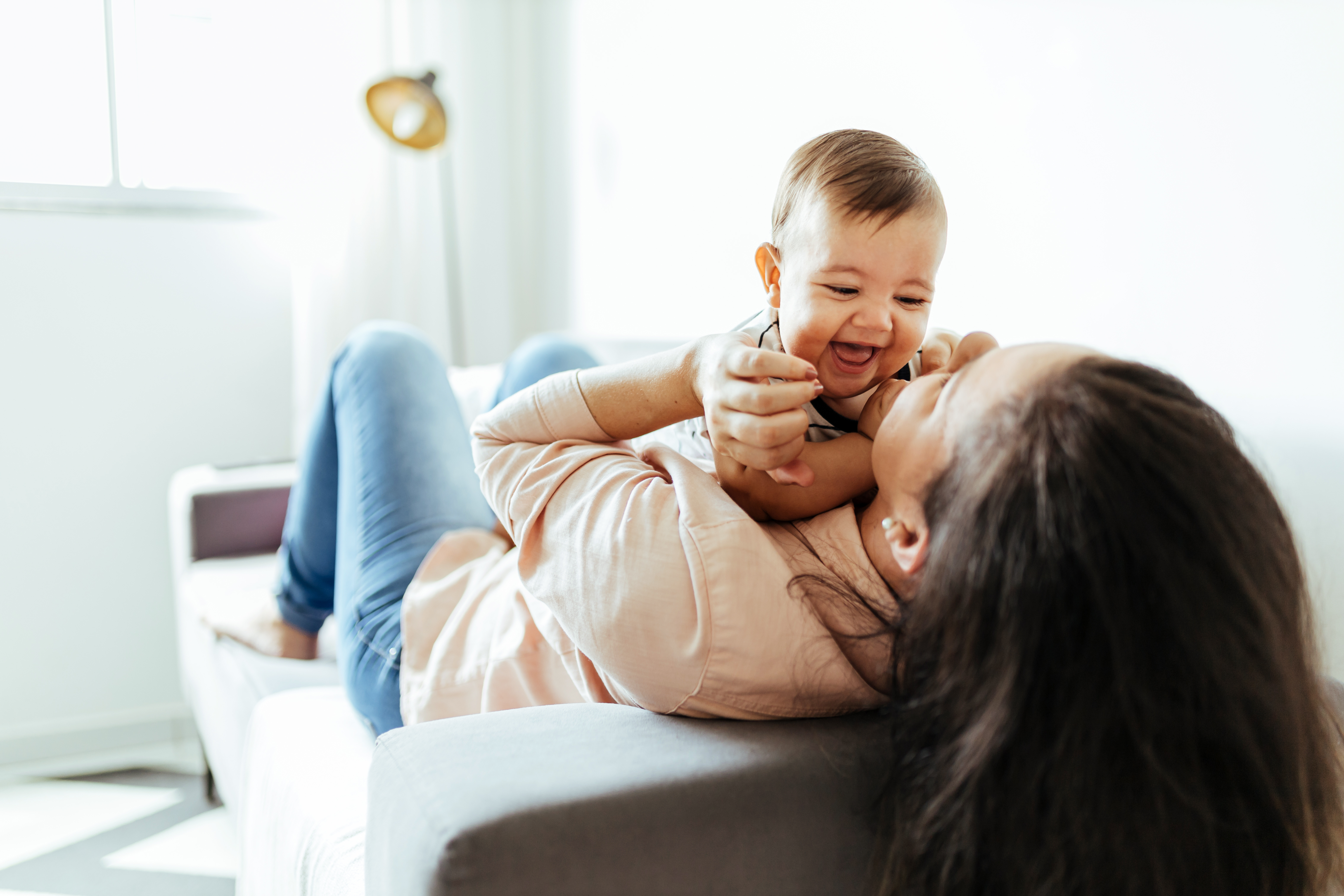 Mother laughing while playing with her baby on the sofa