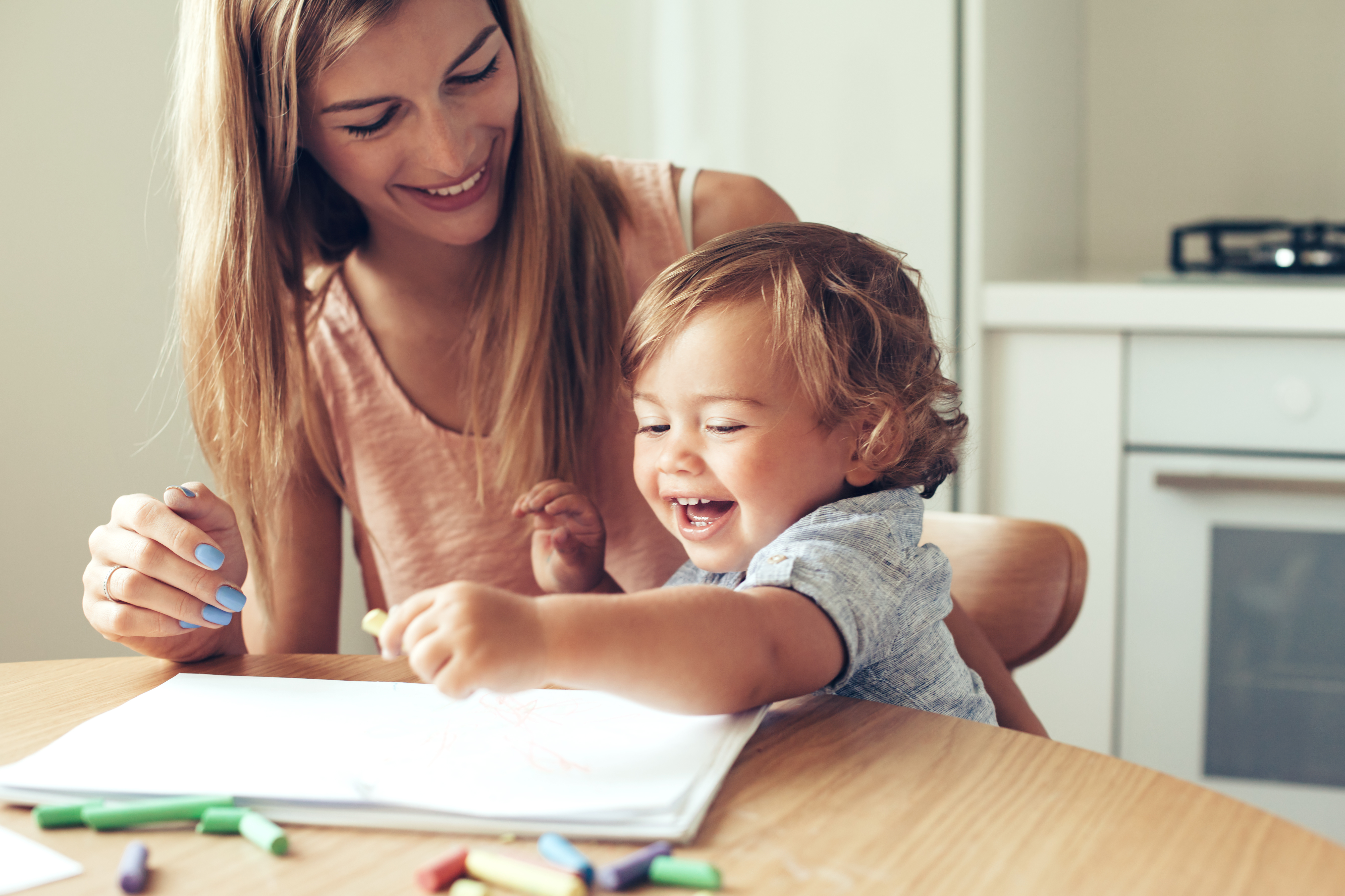 Mother watching her toddler draw at a kitchen table