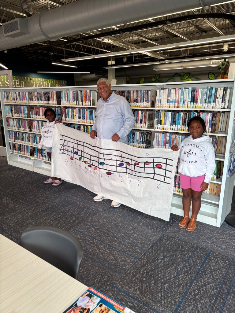 Mentor and students holding a hand-painted music note banner