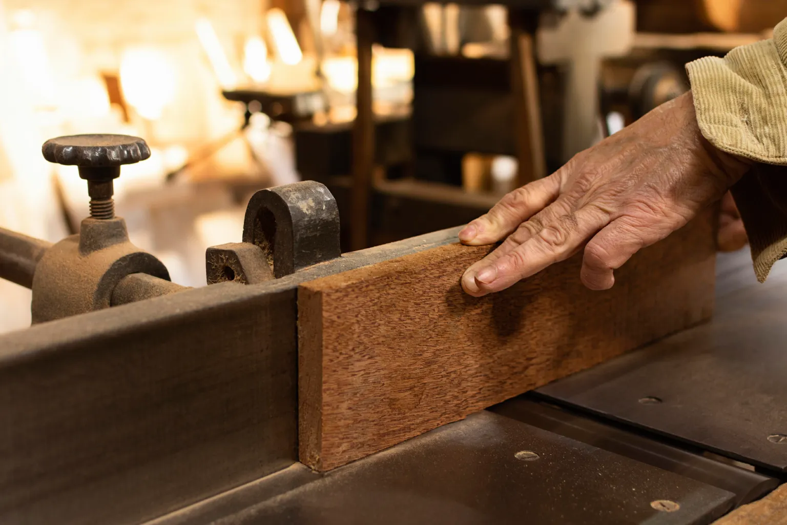 Woodworker pressing a piece of mahogany hardwood against a jointer fence in a workshop