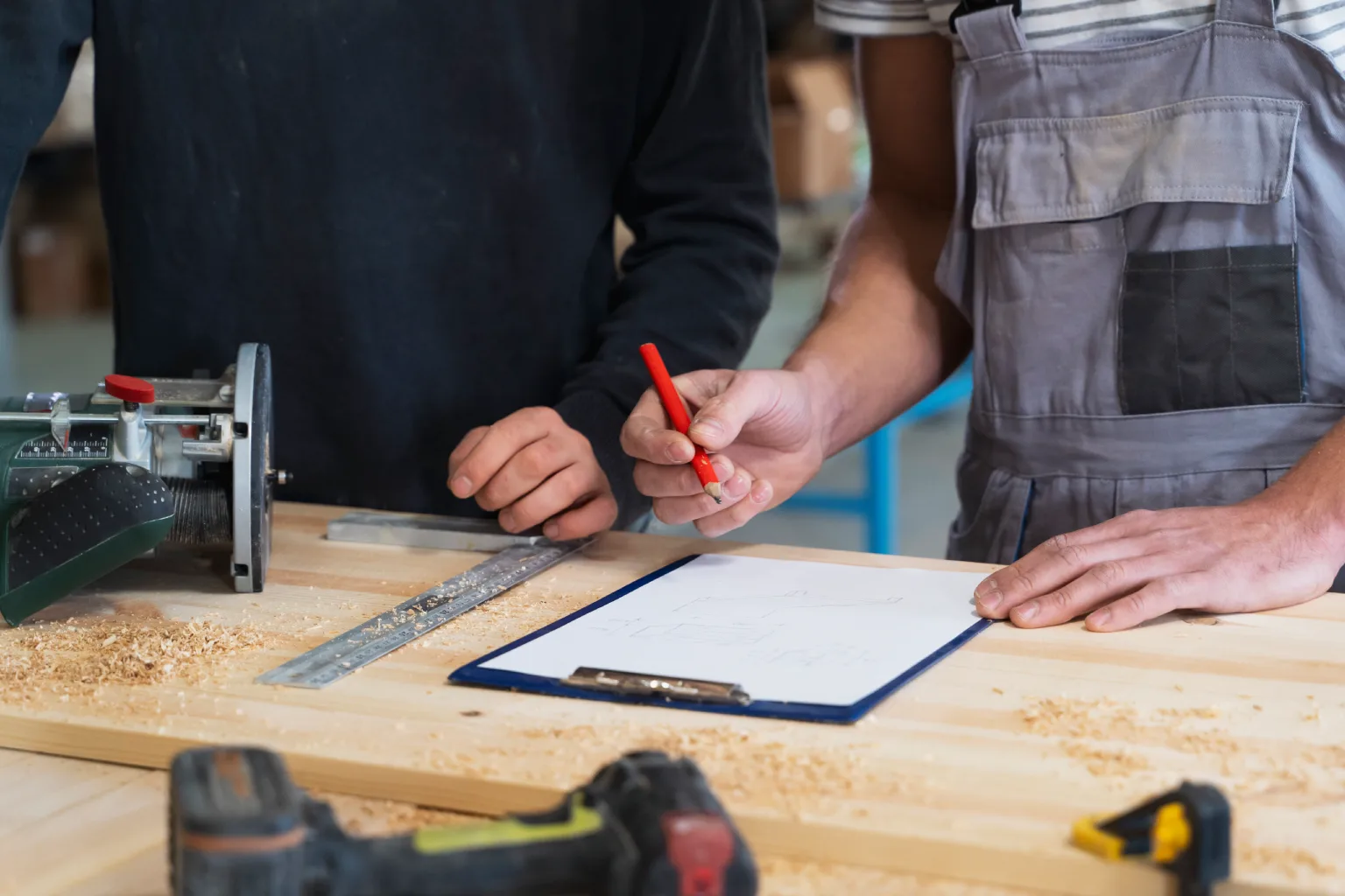 Two people in a workshop reviewing notes on a clipboard over a wooden workbench