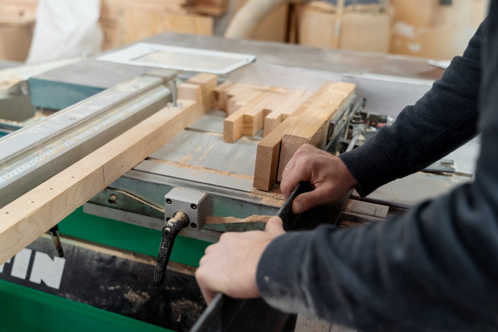 Woodworker guiding material along a table saw fence in a workshop