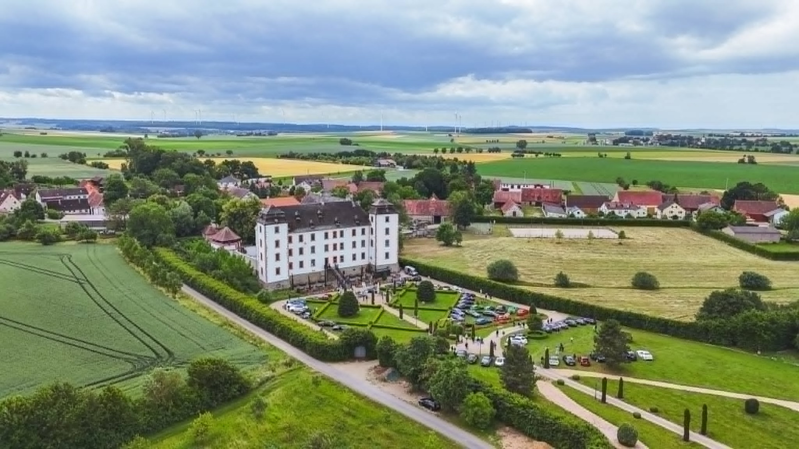 Luftbild des Schlosses mit Autotreffen im Barockgarten und umliegenden Feldern