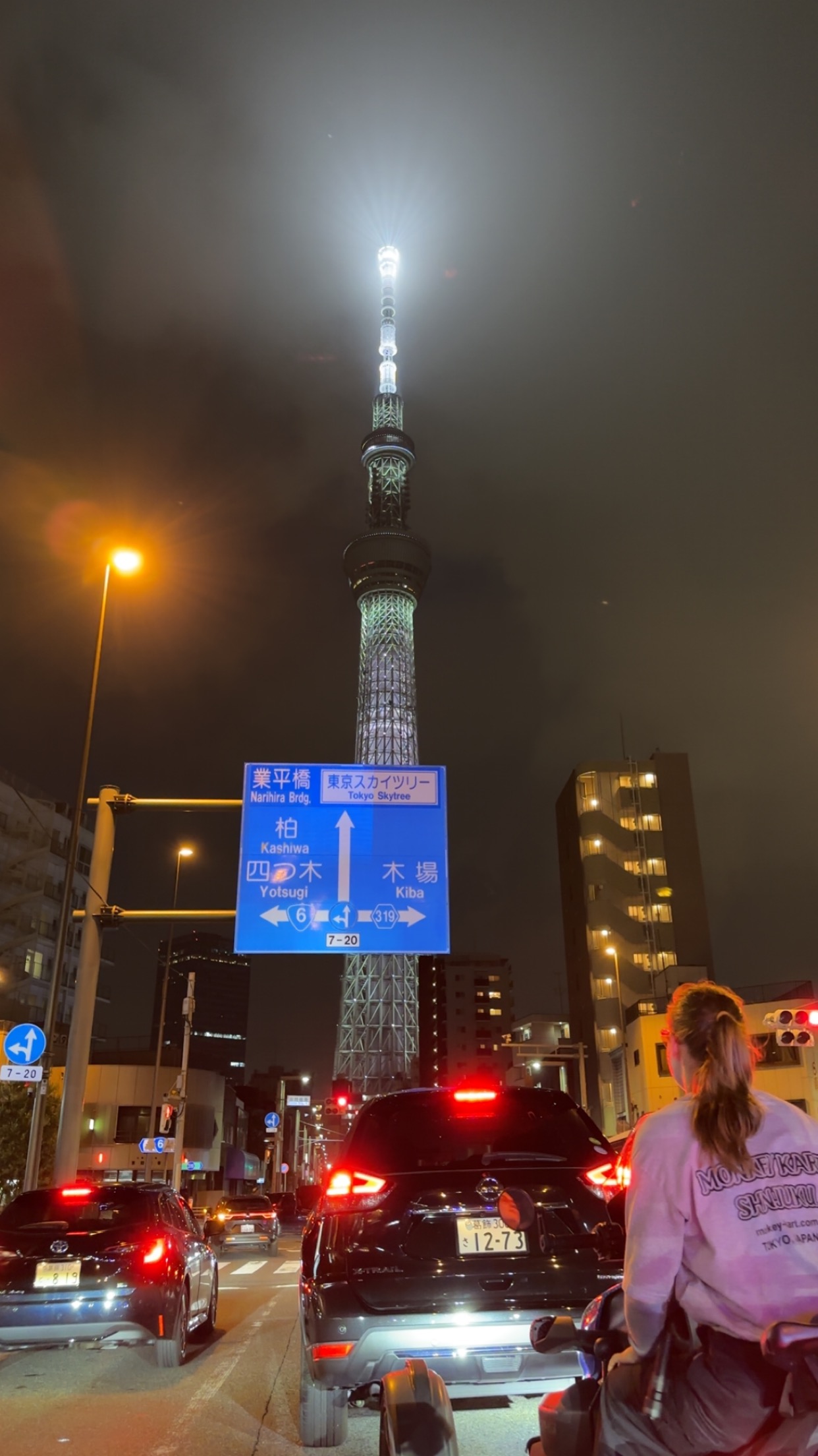Night-time view from a go-kart of a blue Tokyo street sign pointing toward Tokyo Skytree