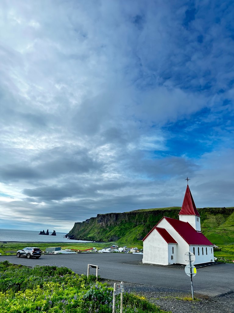 A black church in Iceland surrounded by green hills