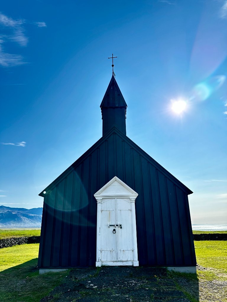 The black Búðir church in Iceland under a bright blue sky