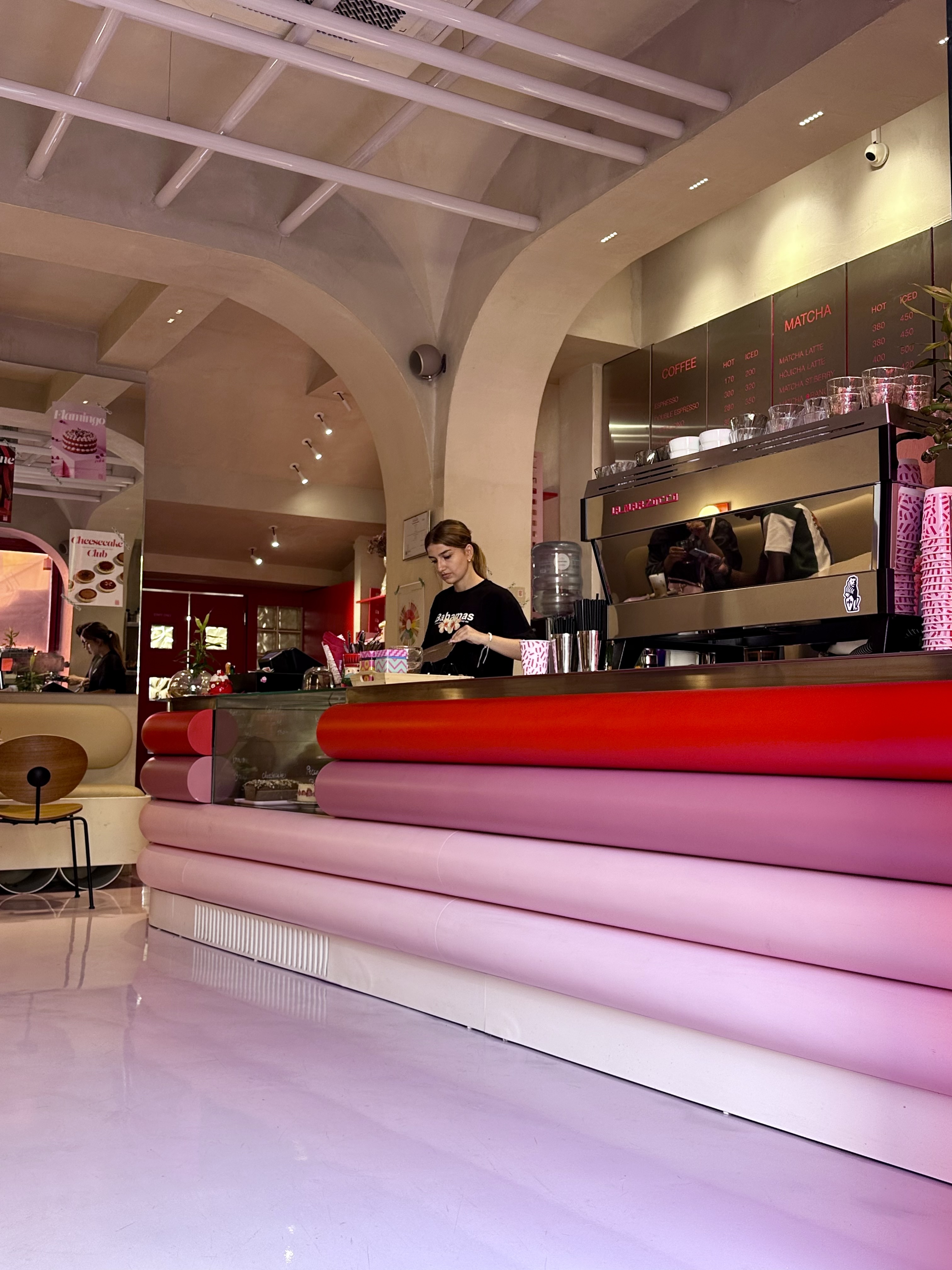 Café interior with a pink gradient counter and menu board in Tirana