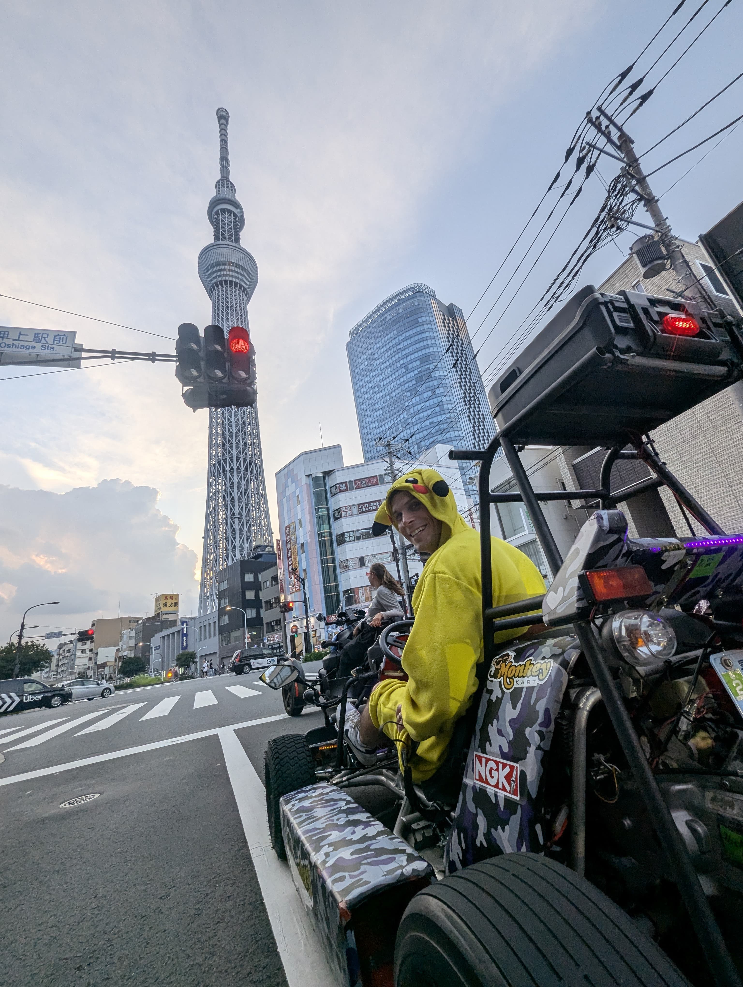 Driver in a yellow Pikachu onesie and another driver in a pink leopard-print go-kart, with the Tokyo Skytree in the background