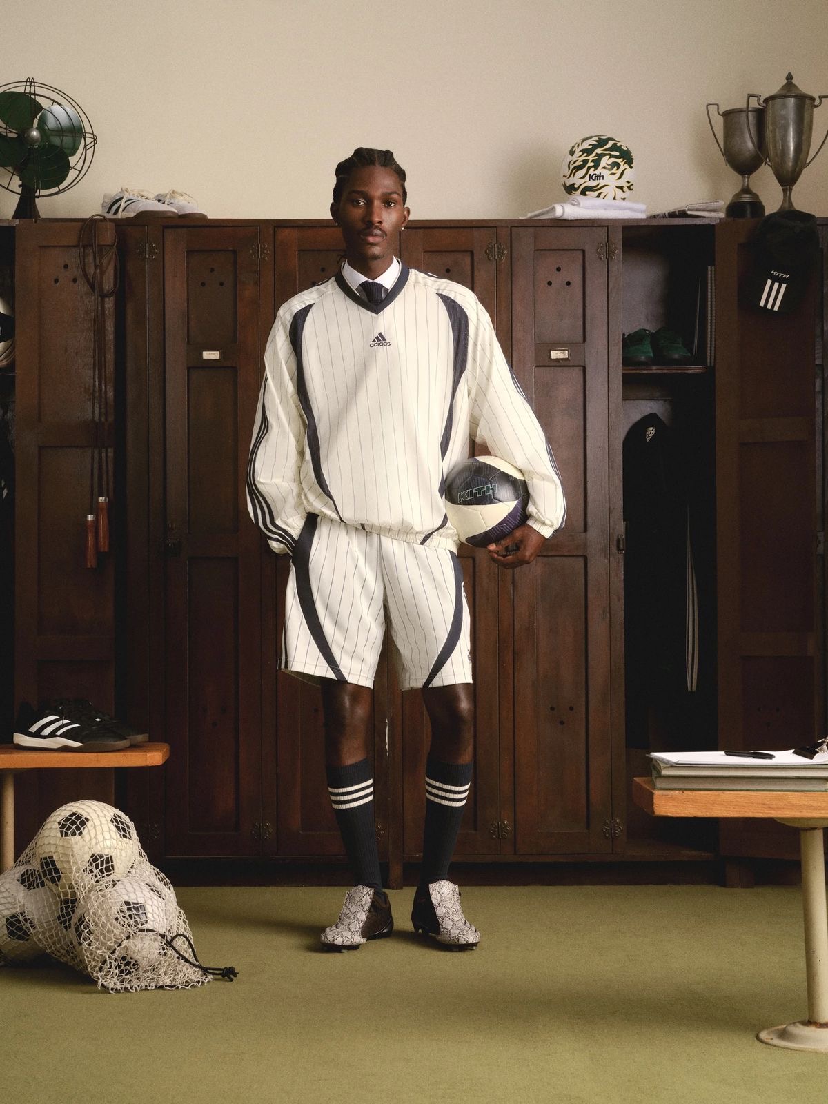 Model in a cream pinstripe football kit holding a ball in a vintage locker room