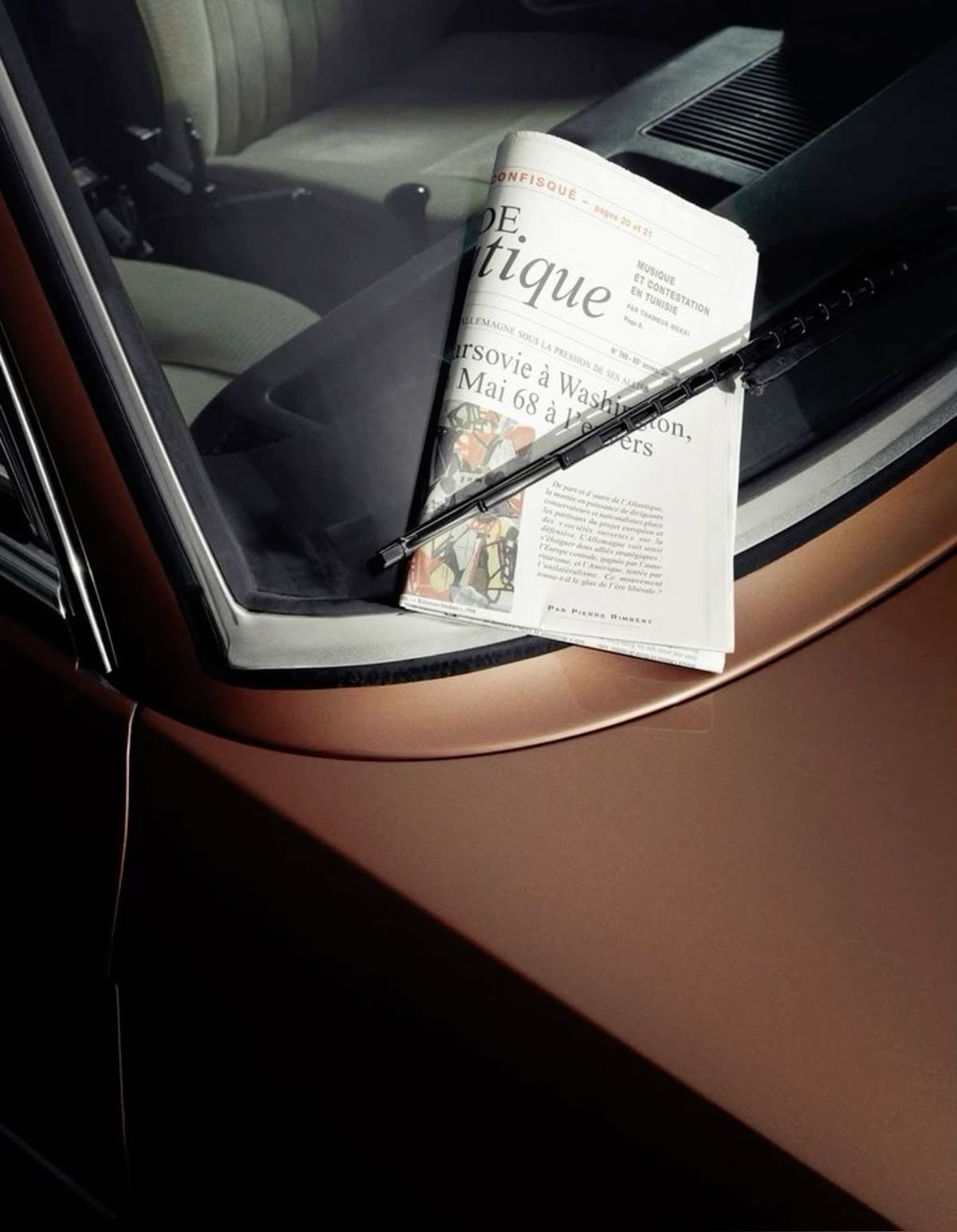French newspaper resting on the windshield of a copper-toned car