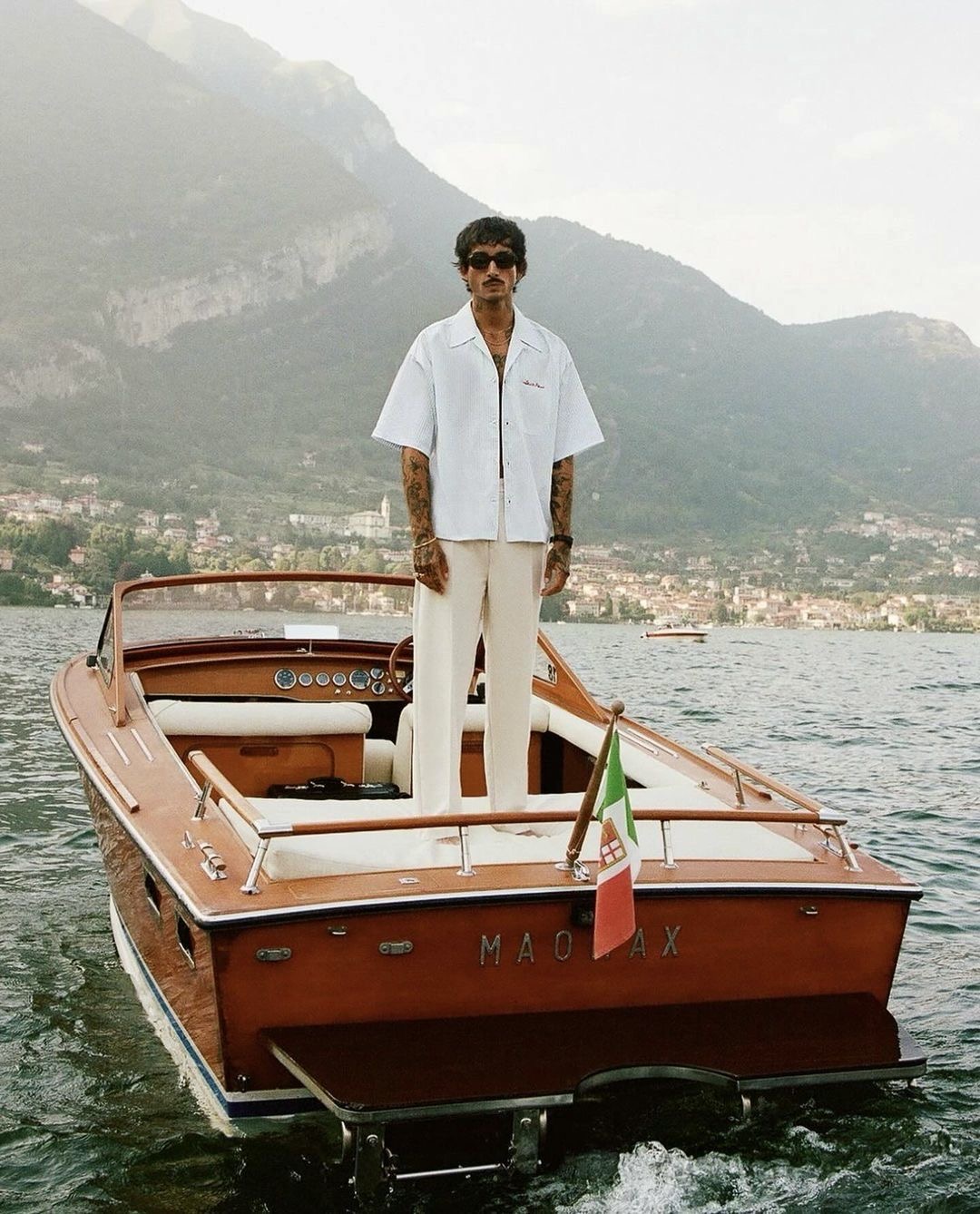 Man standing aboard a wooden runabout on an alpine lake