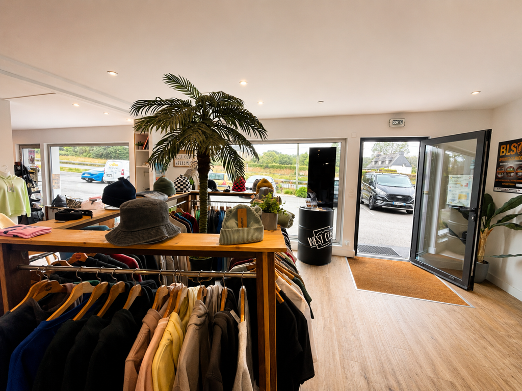 Espace de vente West Cust avec racks de vêtements, table central de bonnets et chapeaux