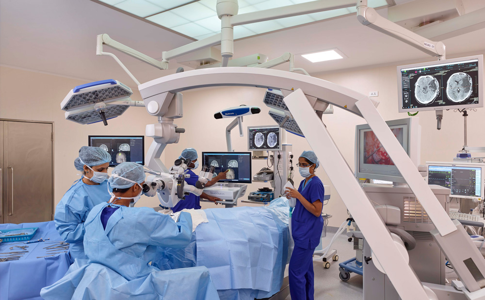 Meitra Hospital modern operating theatre with surgical microscope, high-resolution monitors displaying diagnostic imaging, and surgical team in blue scrubs.