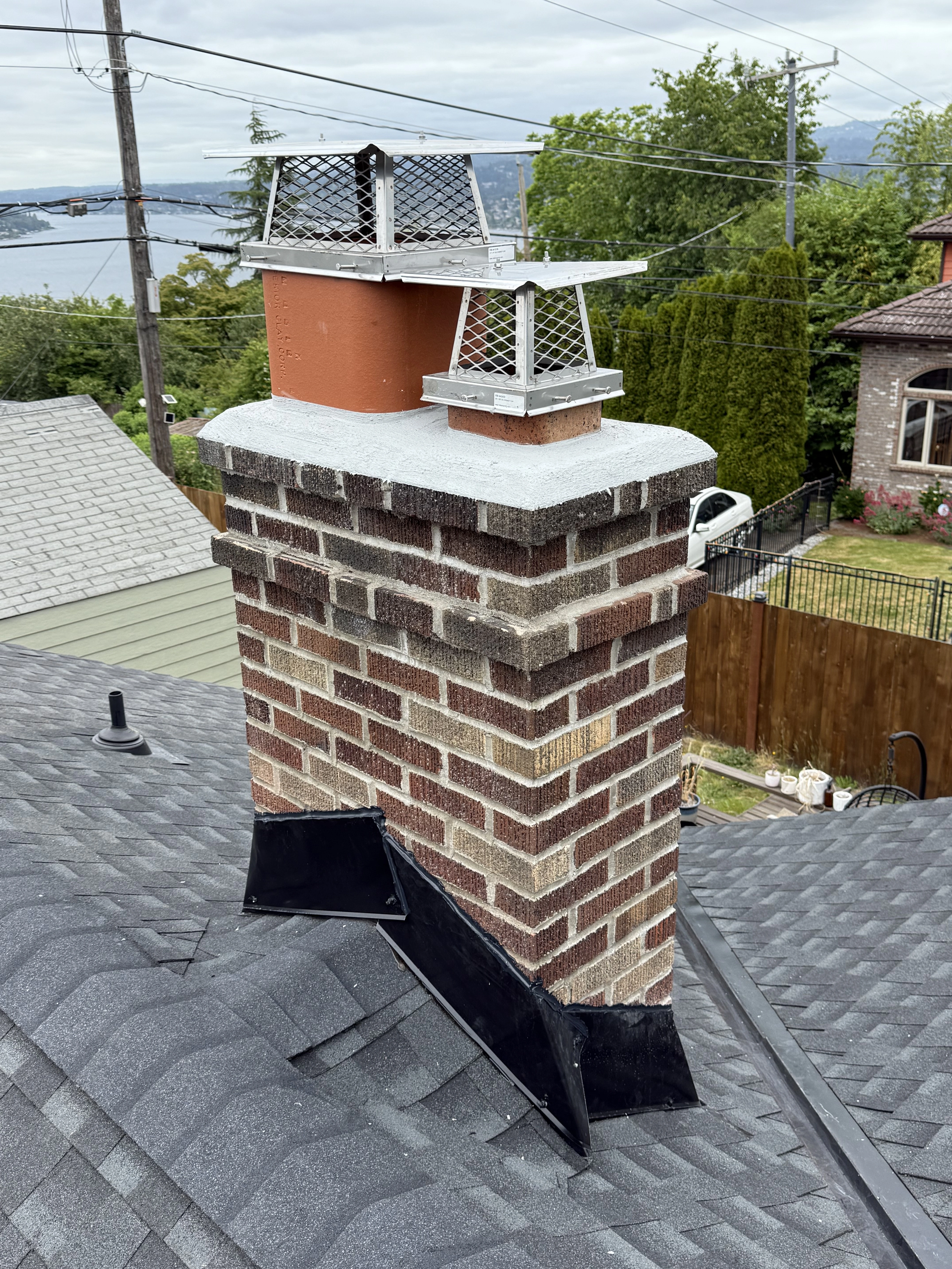 Brick chimney with new flashing installation and stainless steel caps on Seattle area roof