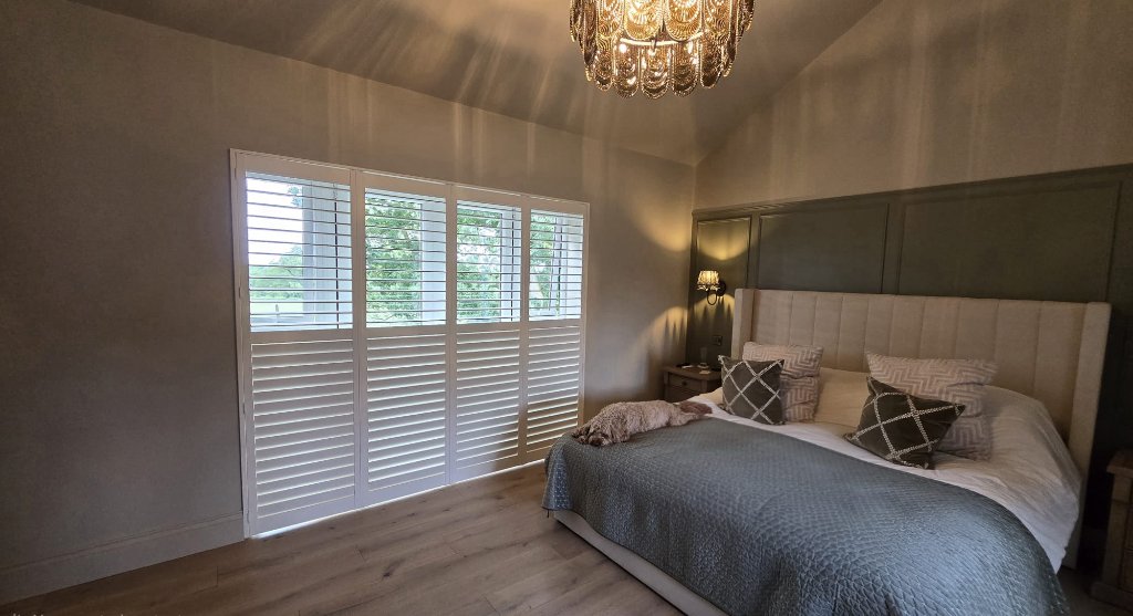 White plantation shutters fitted on floor-to-ceiling windows in a Harrogate bedroom