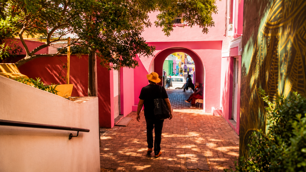 Sunlit pedestrian alleyway in Bo-Kaap, Cape Town with vibrant pink walls leading toward an arched stone doorway