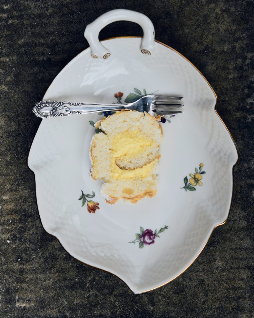 Stykke blød kage med vaniljecreme på blomstret porcelænsfad