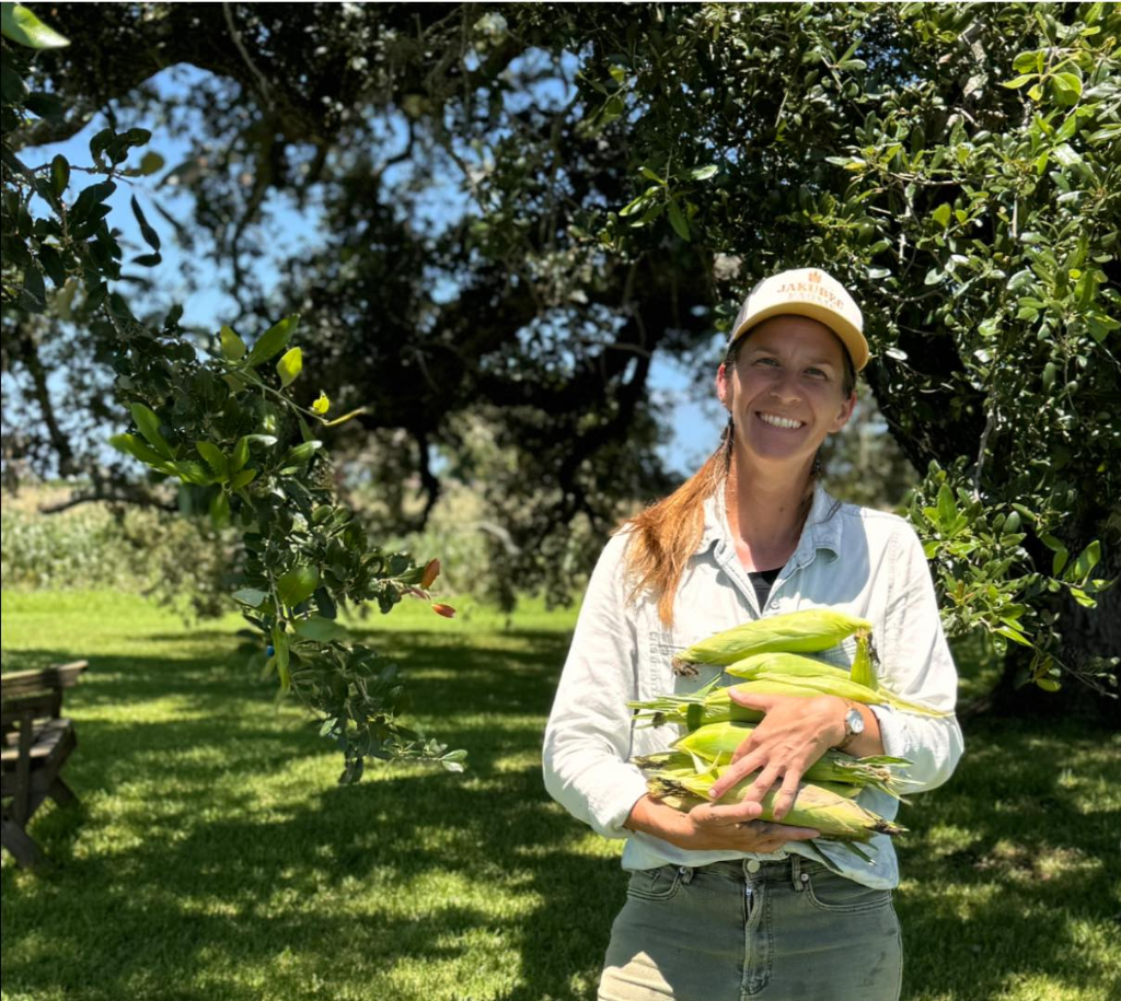 Farm instructor holding fresh sweet corn under the trees