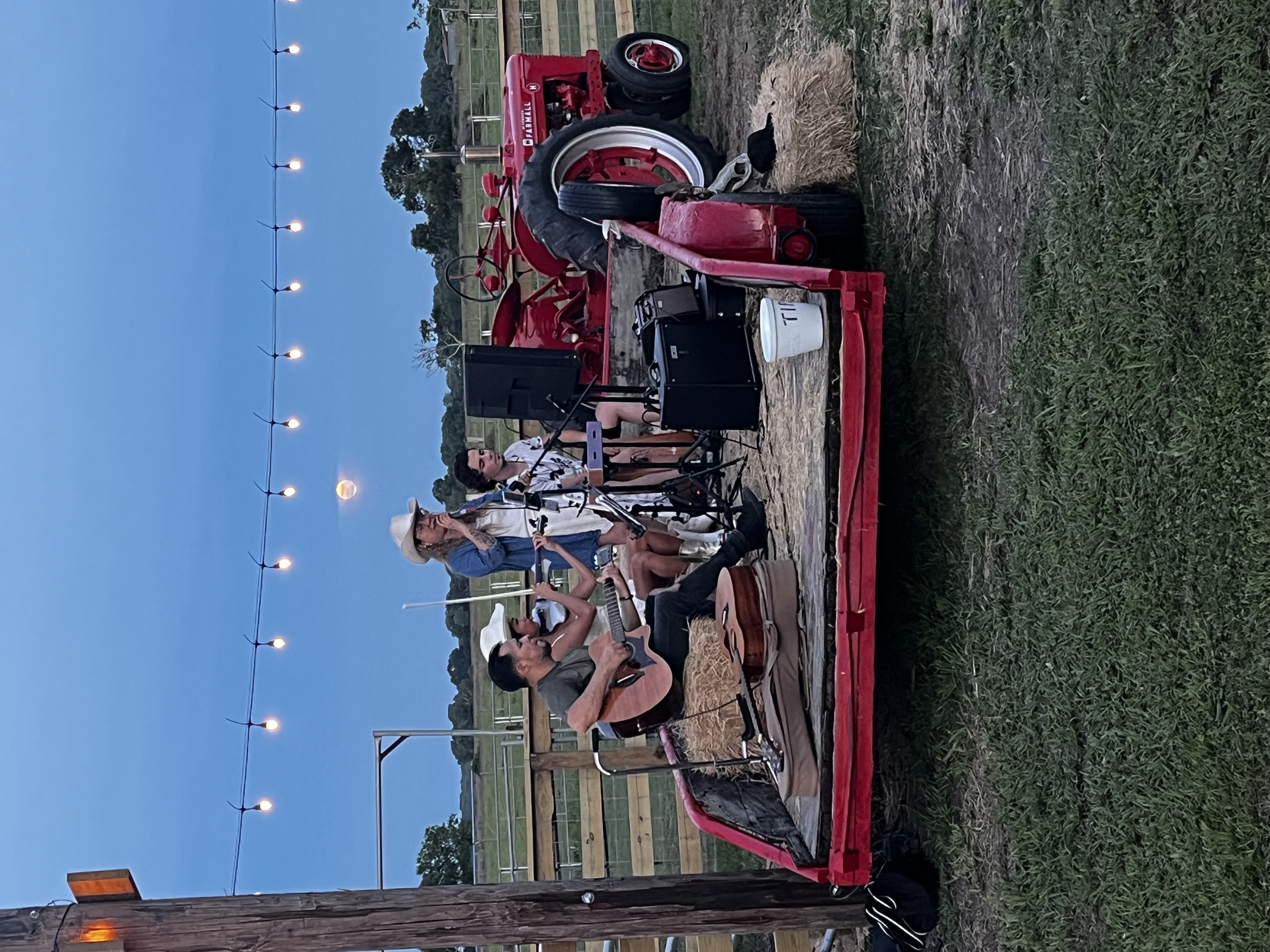 Live country music on a flatbed trailer under string lights at twilight on Heart Rock Farm