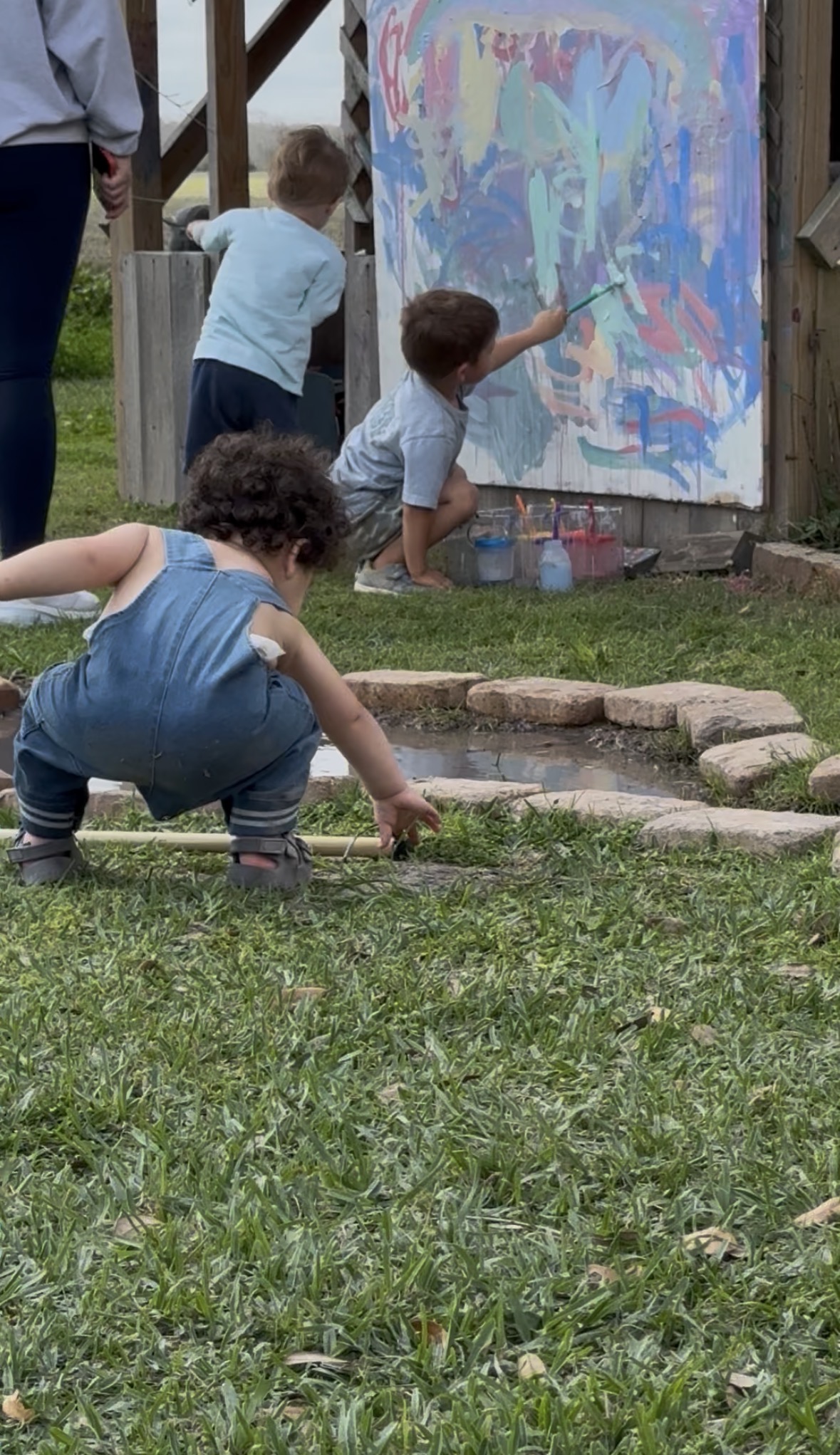 Children painting on a large outdoor easel by the mud puddle