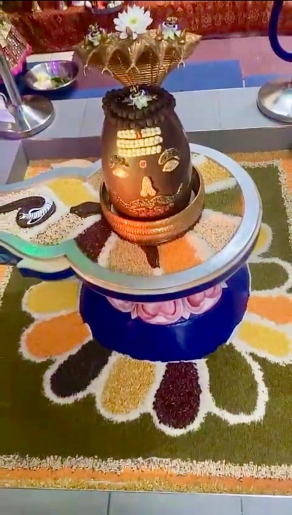 An ornate grain-art rangoli surrounds the beautifully decorated Lingam.