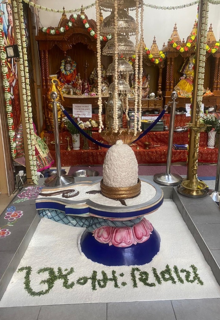 Om Namah Shivaya inscribed in greenery beside the rice-adorned Lingam.