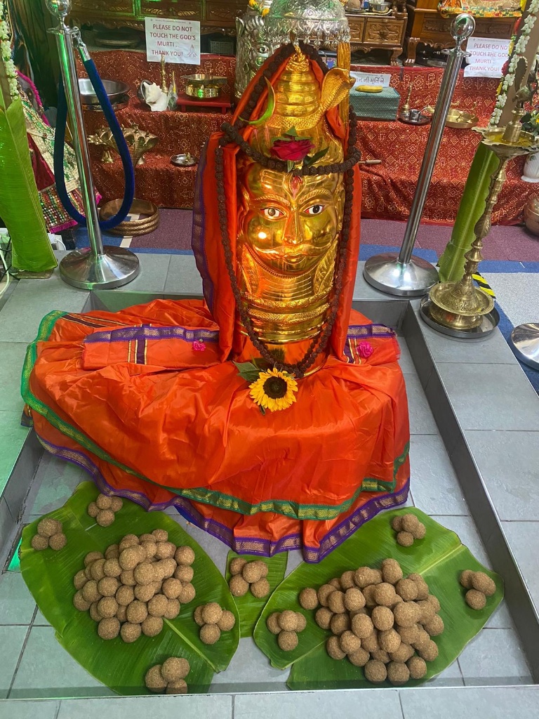 Golden face shringar with offerings of laddus on banana leaves.