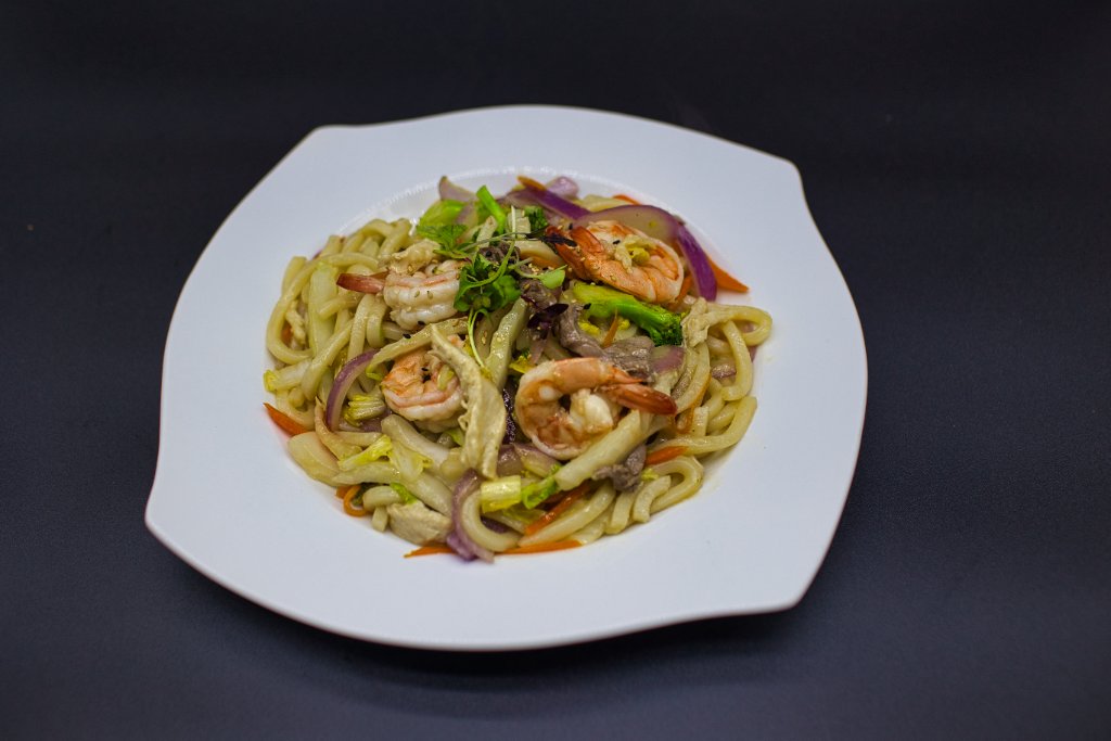 Shrimp udon noodles with vegetables on white plate
