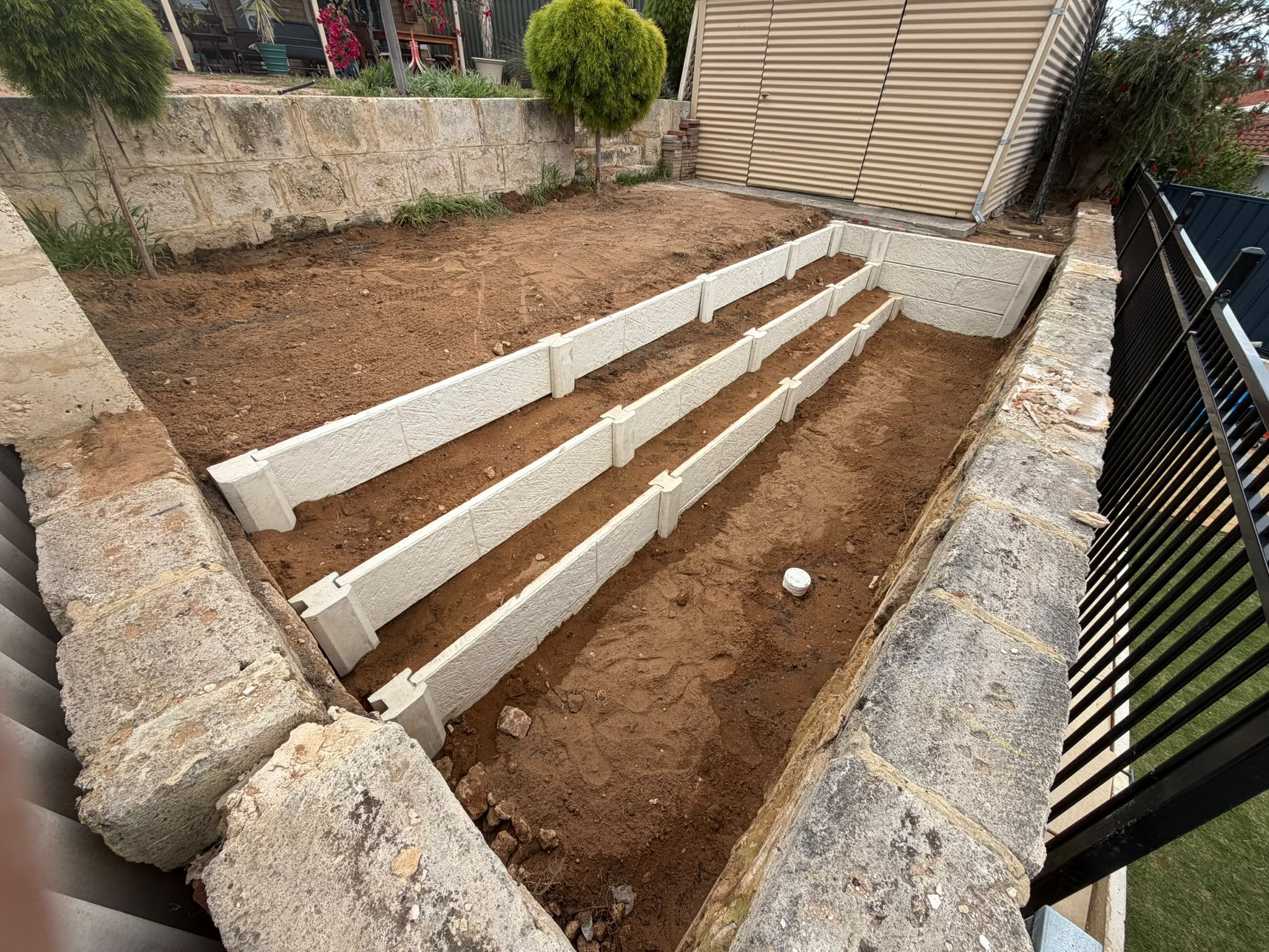 Tiered concrete sleeper garden bed walls under construction