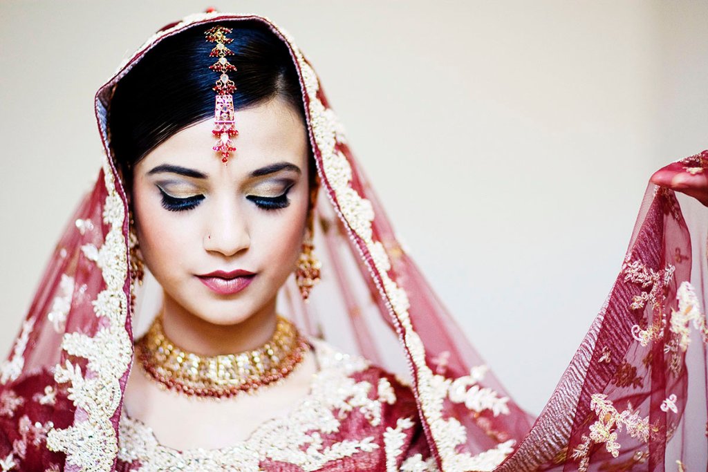 A South Asian bride in a deep maroon embroidered veil, eyes closed in a quiet moment
