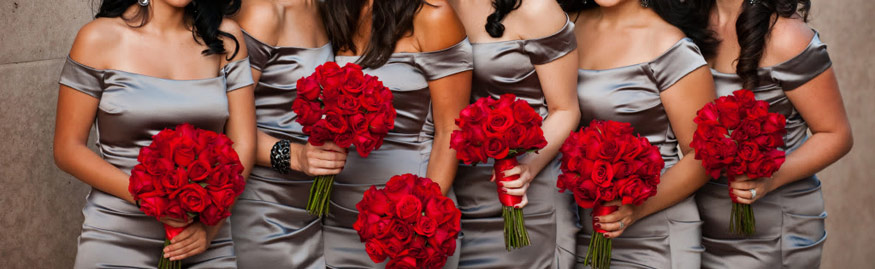 Six bridesmaids in silver-grey satin dresses holding bouquets of deep red roses