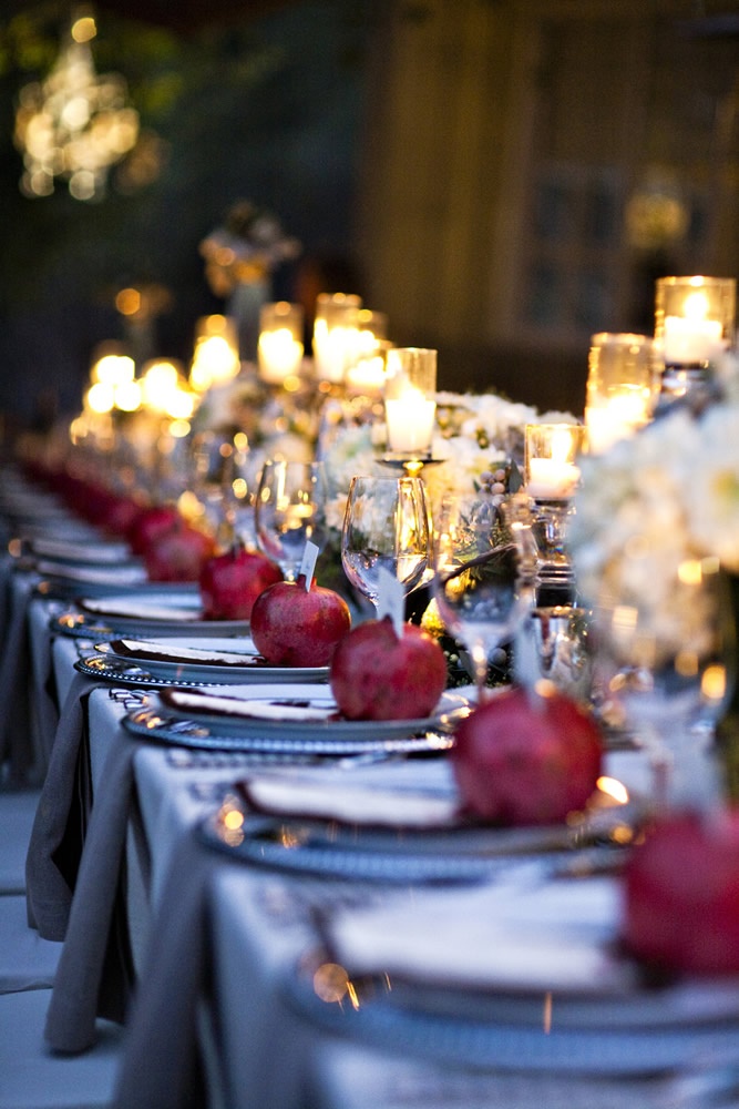 A long candlelit reception table set with pomegranates, white florals and warm votives at dusk