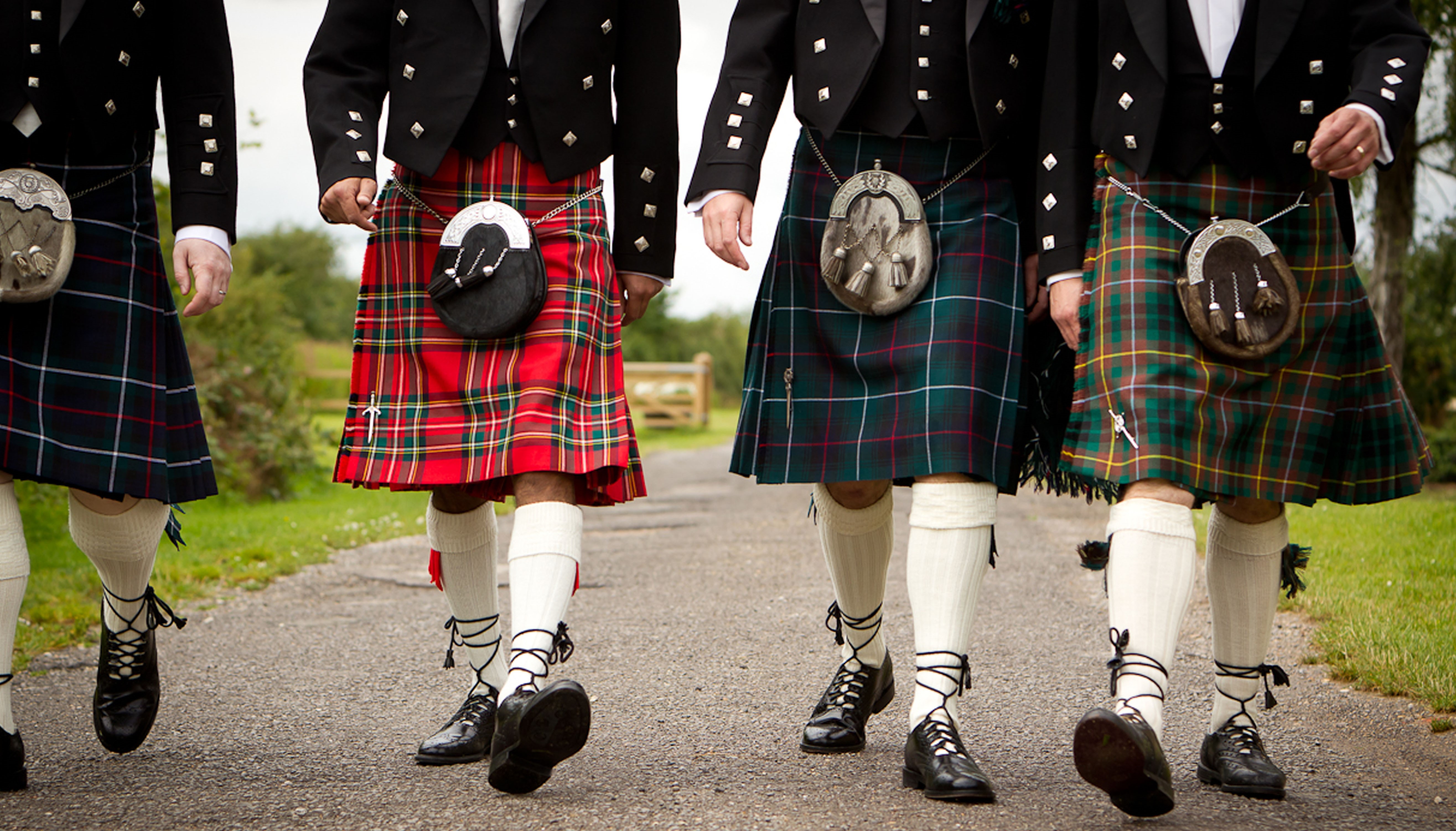 A wedding party in formal Highland dress walking together toward the celebration