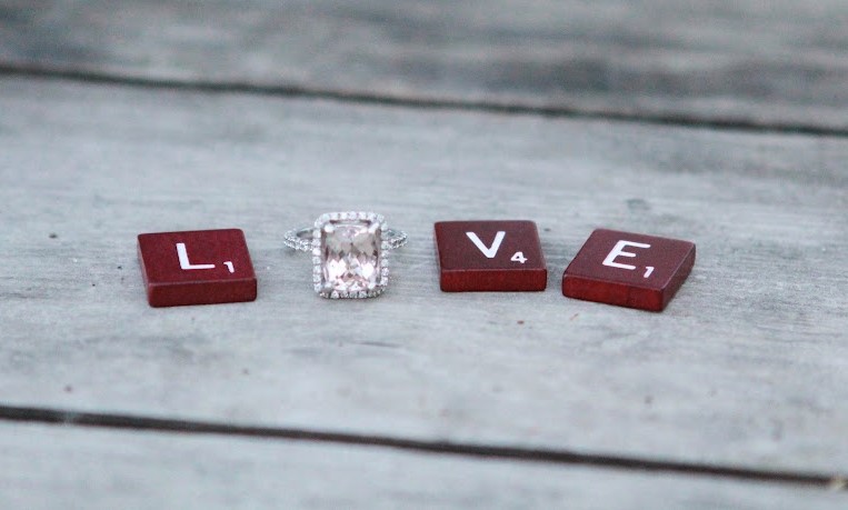 Scrabble tiles spelling LOVE, with a diamond engagement ring in place of the letter O