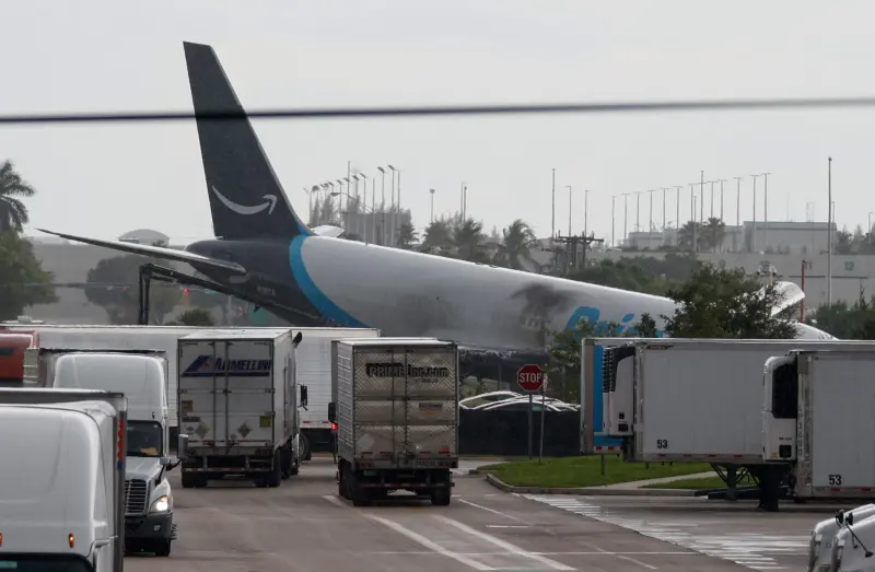 Amazon Prime Air cargo jet with scorch marks on fuselage near semi-trucks